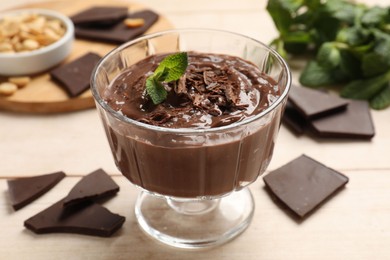 Photo of Tasty pudding with mint and pieces of chocolate on white wooden table, closeup