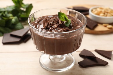 Photo of Tasty pudding with mint and pieces of chocolate on white wooden table, closeup