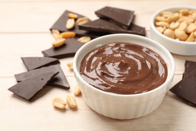 Photo of Tasty pudding, pieces of chocolate and peanuts on white wooden table, closeup