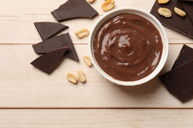 Photo of Tasty pudding, pieces of chocolate and peanuts on white wooden table, flat lay