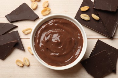 Photo of Tasty pudding, pieces of chocolate and peanuts on white wooden table, flat lay