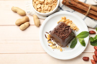 Photo of Tasty chocolate pudding with peanuts and mint on white wooden table, flat lay