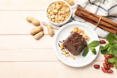 Photo of Tasty chocolate pudding with peanuts and mint on white wooden table, flat lay