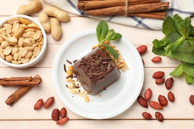 Photo of Tasty chocolate pudding with peanuts and mint on white wooden table, flat lay