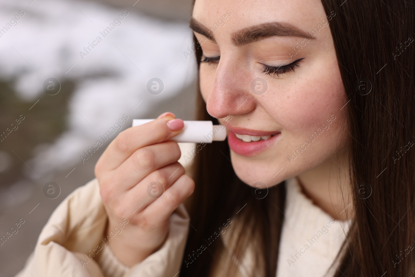 Photo of Beautiful young woman applying lip balm outdoors