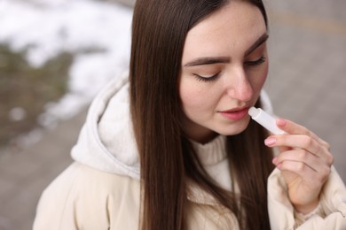 Photo of Beautiful young woman applying lip balm on winter day