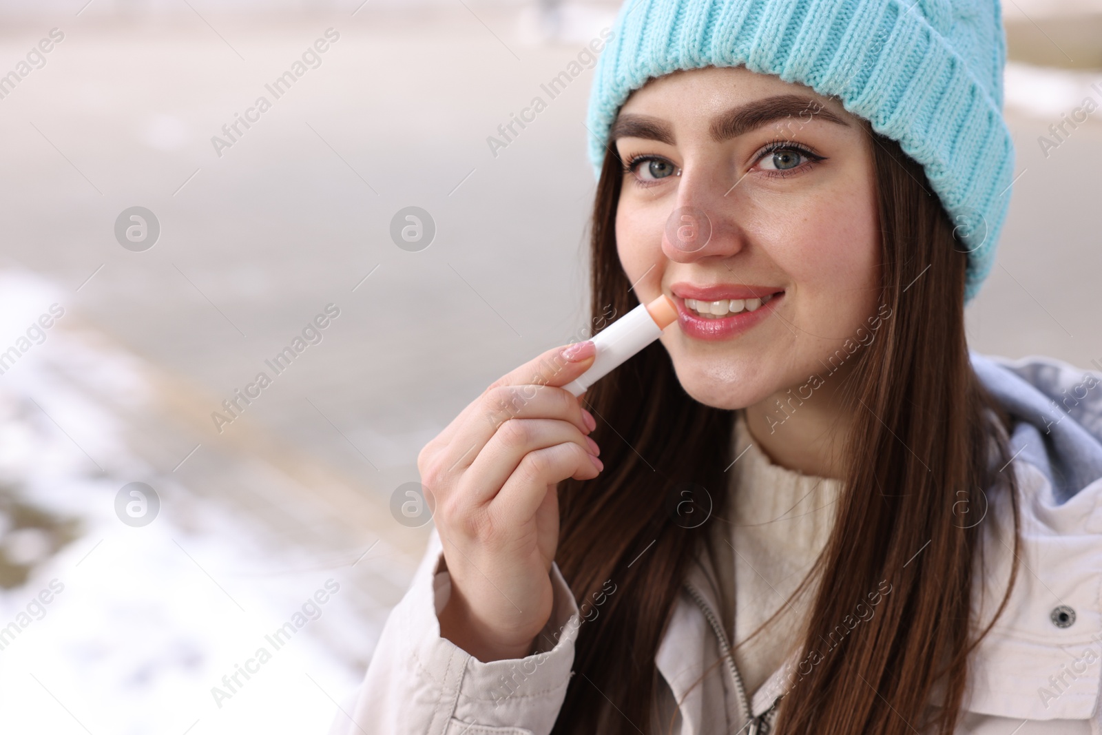 Photo of Beautiful young woman applying lip balm on winter day. Space for text