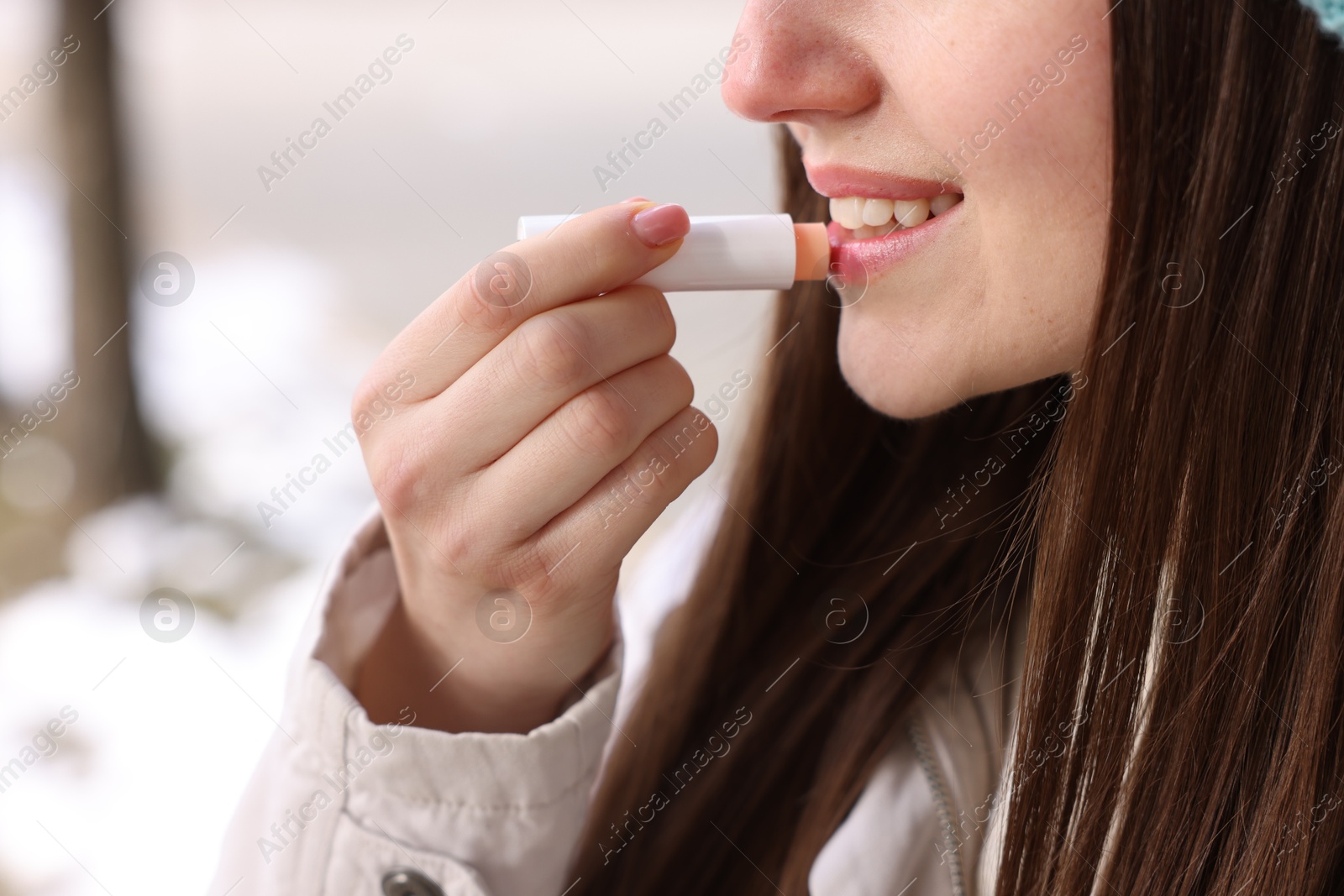 Photo of Young woman applying lip balm outdoors, closeup