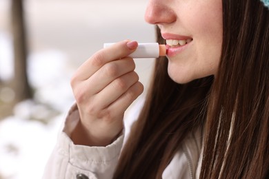 Photo of Young woman applying lip balm outdoors, closeup