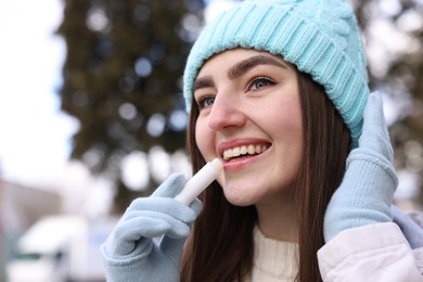 Photo of Beautiful young woman applying lip balm on winter day