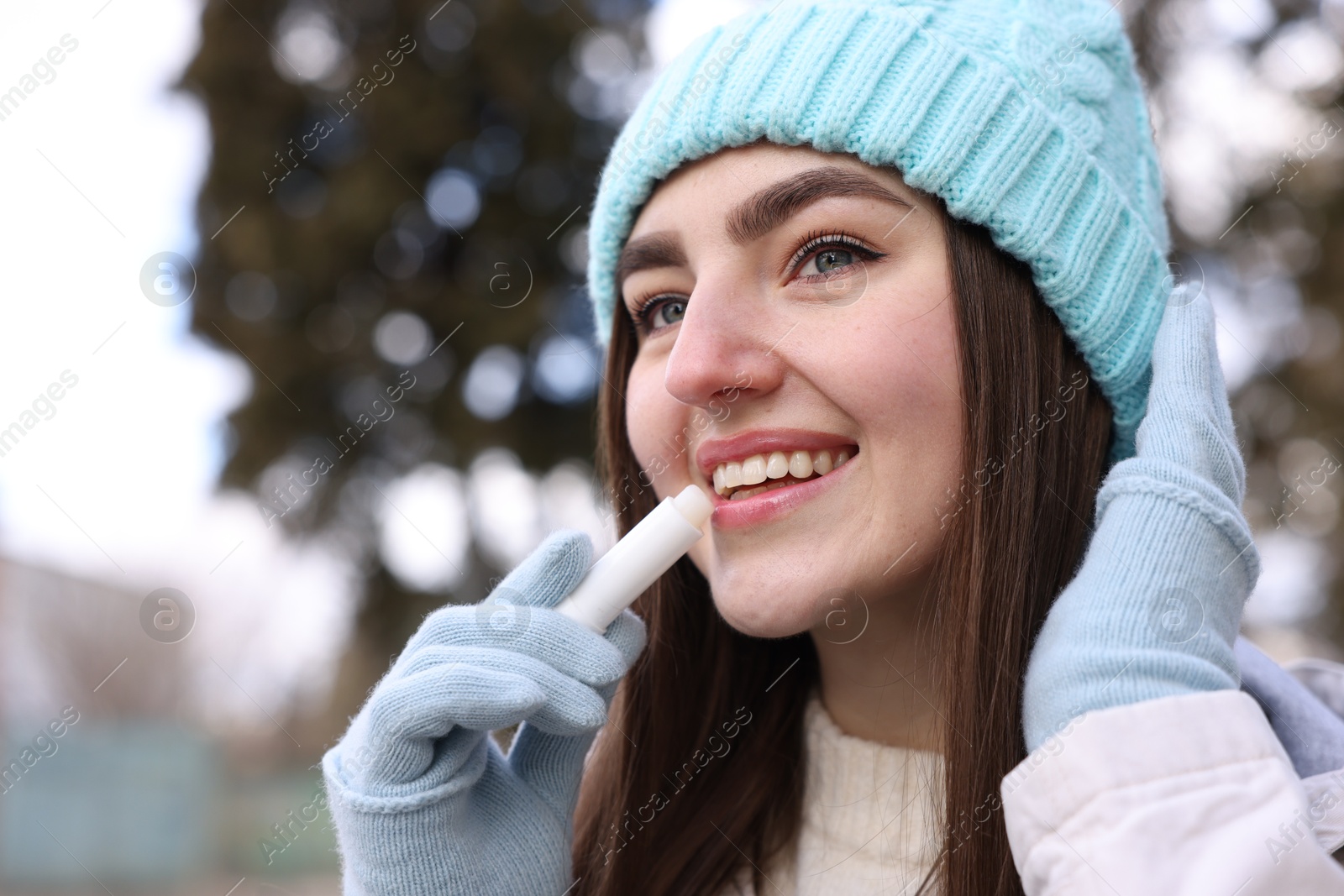 Photo of Beautiful young woman applying lip balm on winter day