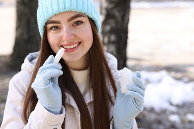 Photo of Beautiful young woman applying lip balm on winter day