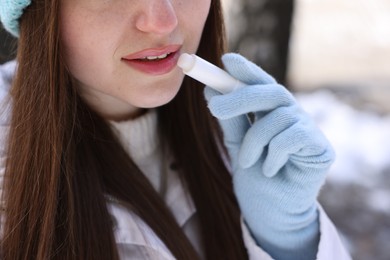 Photo of Young woman applying lip balm outdoors, closeup