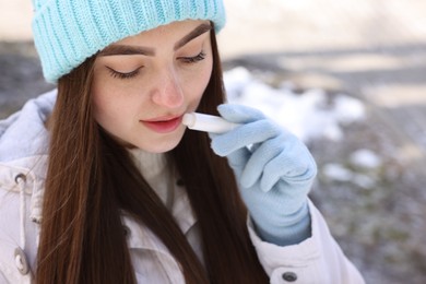 Beautiful young woman applying lip balm on winter day