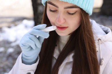 Photo of Beautiful young woman applying lip balm on winter day