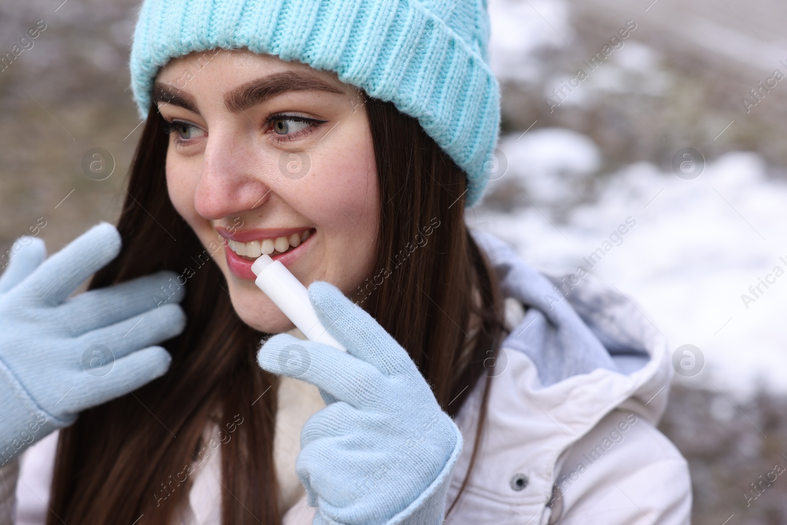 Photo of Beautiful young woman applying lip balm on winter day