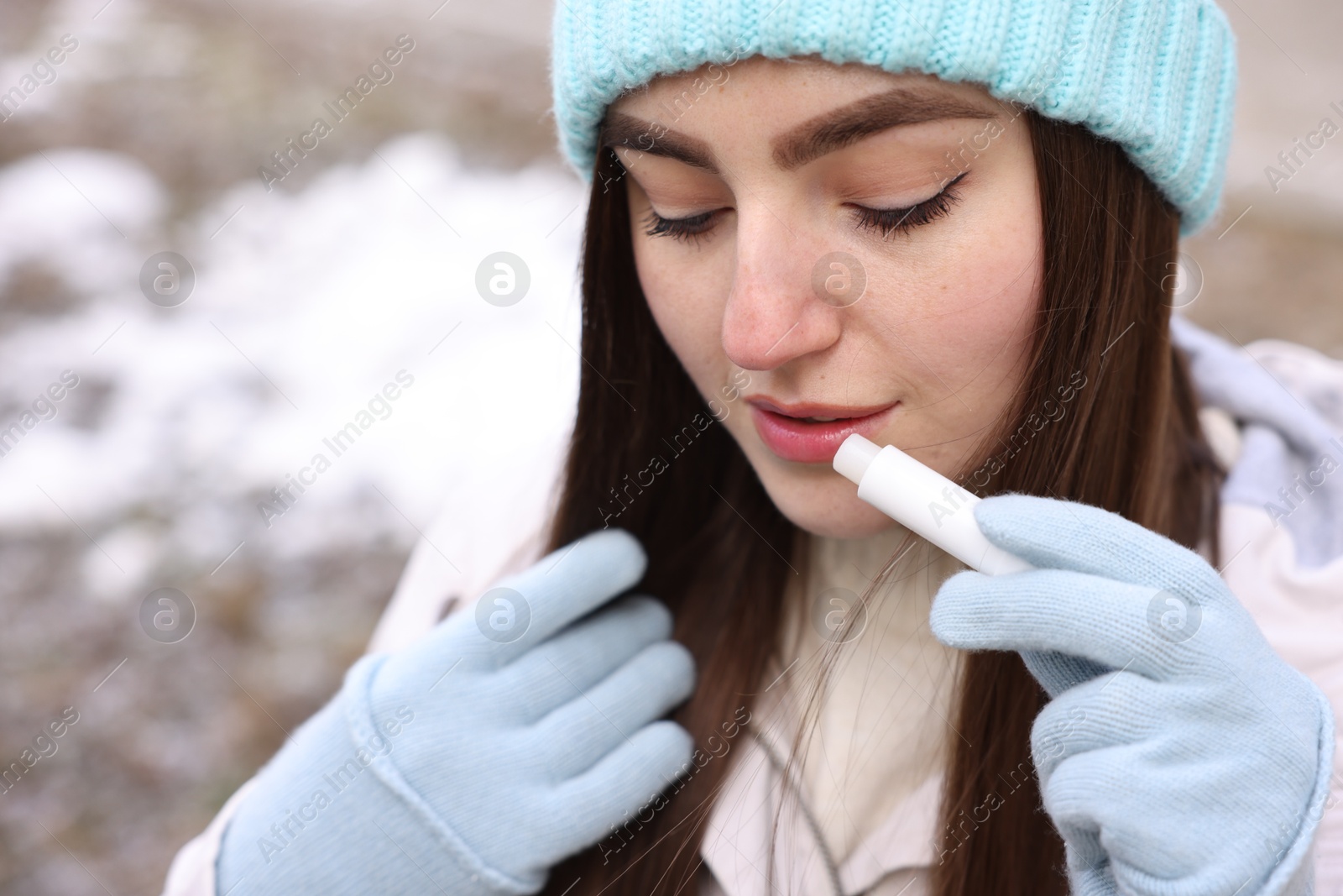 Photo of Beautiful young woman applying lip balm on winter day