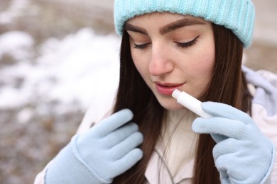 Photo of Beautiful young woman applying lip balm on winter day