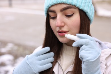 Photo of Beautiful young woman applying lip balm on winter day