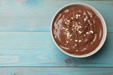 Photo of Tasty chocolate pudding in bowl on light blue wooden table, top view. Space for text