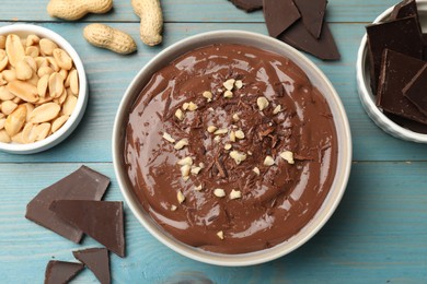 Photo of Tasty chocolate pudding in bowl and ingredients on light blue wooden table, flat lay