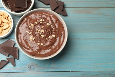 Photo of Tasty chocolate pudding in bowl and ingredients on light blue wooden table, flat lay. Space for text