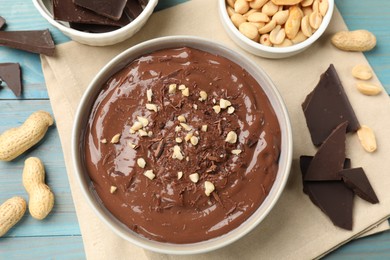 Photo of Tasty chocolate pudding in bowl and ingredients on light blue wooden table, flat lay