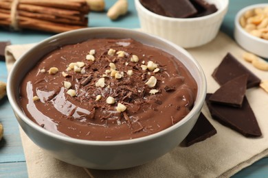 Photo of Tasty chocolate pudding in bowl and ingredients on light blue wooden table, closeup