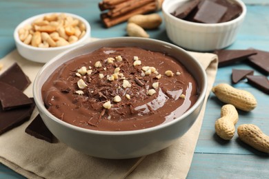 Photo of Tasty chocolate pudding in bowl and ingredients on light blue wooden table, closeup