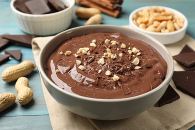 Photo of Tasty chocolate pudding in bowl and ingredients on light blue wooden table, closeup