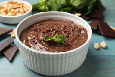 Photo of Tasty chocolate pudding in bowl and ingredients on light blue wooden table, closeup