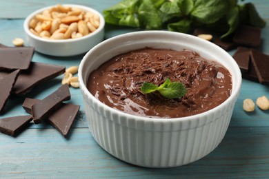 Photo of Tasty chocolate pudding in bowl and ingredients on light blue wooden table, closeup