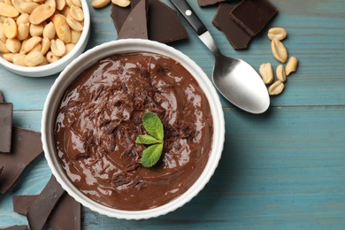 Photo of Tasty chocolate pudding in bowl and ingredients on light blue wooden table, flat lay