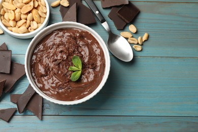 Photo of Tasty chocolate pudding in bowl and ingredients on light blue wooden table, flat lay. Space for text