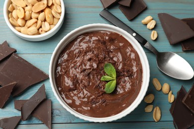 Photo of Tasty chocolate pudding in bowl and ingredients on light blue wooden table, flat lay