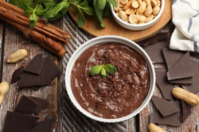 Photo of Tasty chocolate pudding in bowl and ingredients on wooden table, flat lay