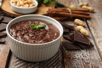 Photo of Tasty chocolate pudding in bowl and ingredients on wooden table, closeup