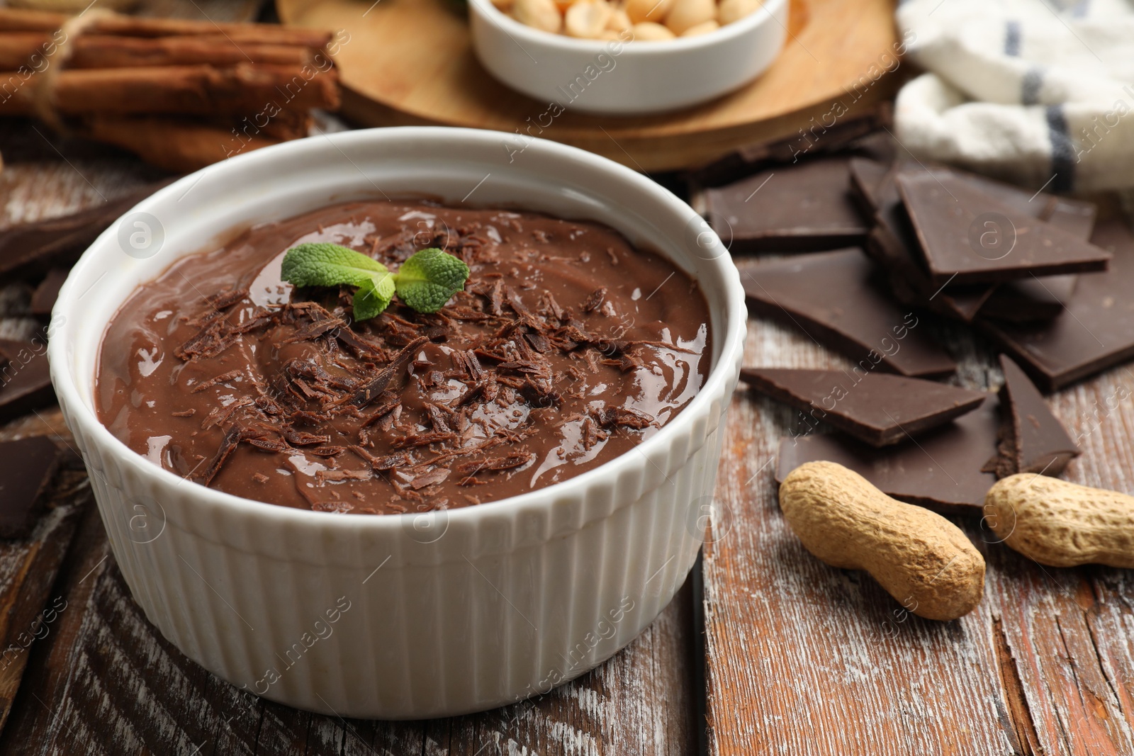 Photo of Tasty chocolate pudding in bowl and ingredients on wooden table, closeup