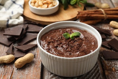 Photo of Tasty chocolate pudding in bowl and ingredients on wooden table, closeup