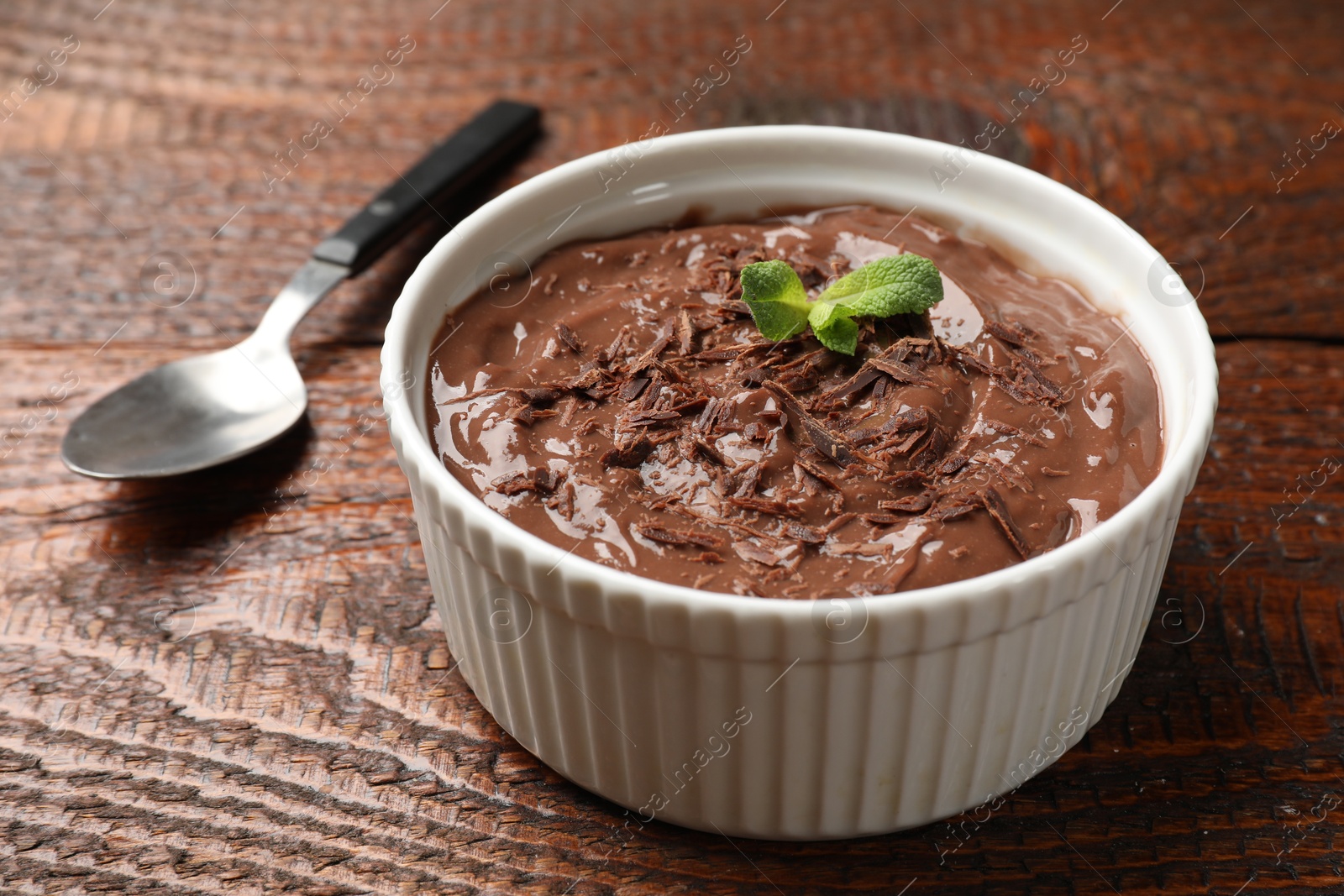 Photo of Tasty chocolate pudding in bowl and spoon on wooden table, closeup