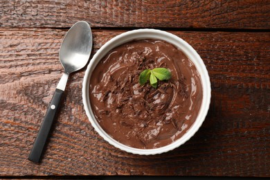 Photo of Tasty chocolate pudding in bowl and spoon on wooden table, top view