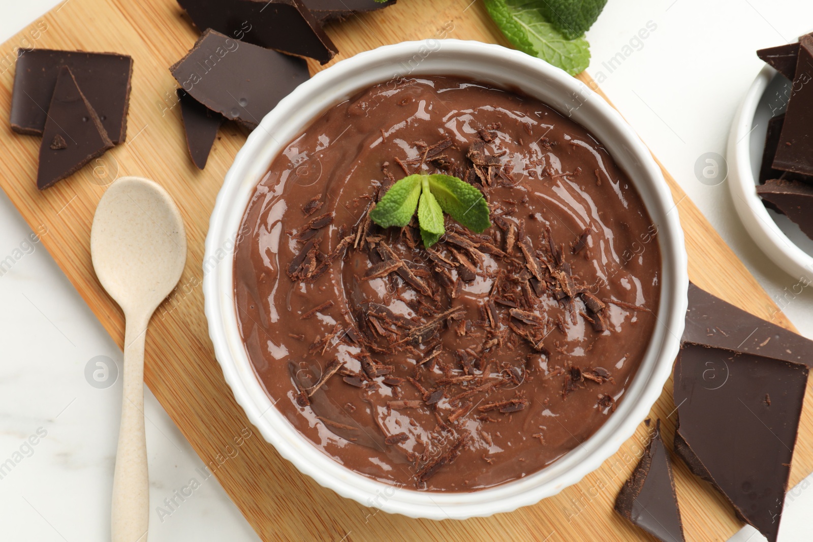 Photo of Tasty chocolate pudding in bowl served on white marble table, flat lay