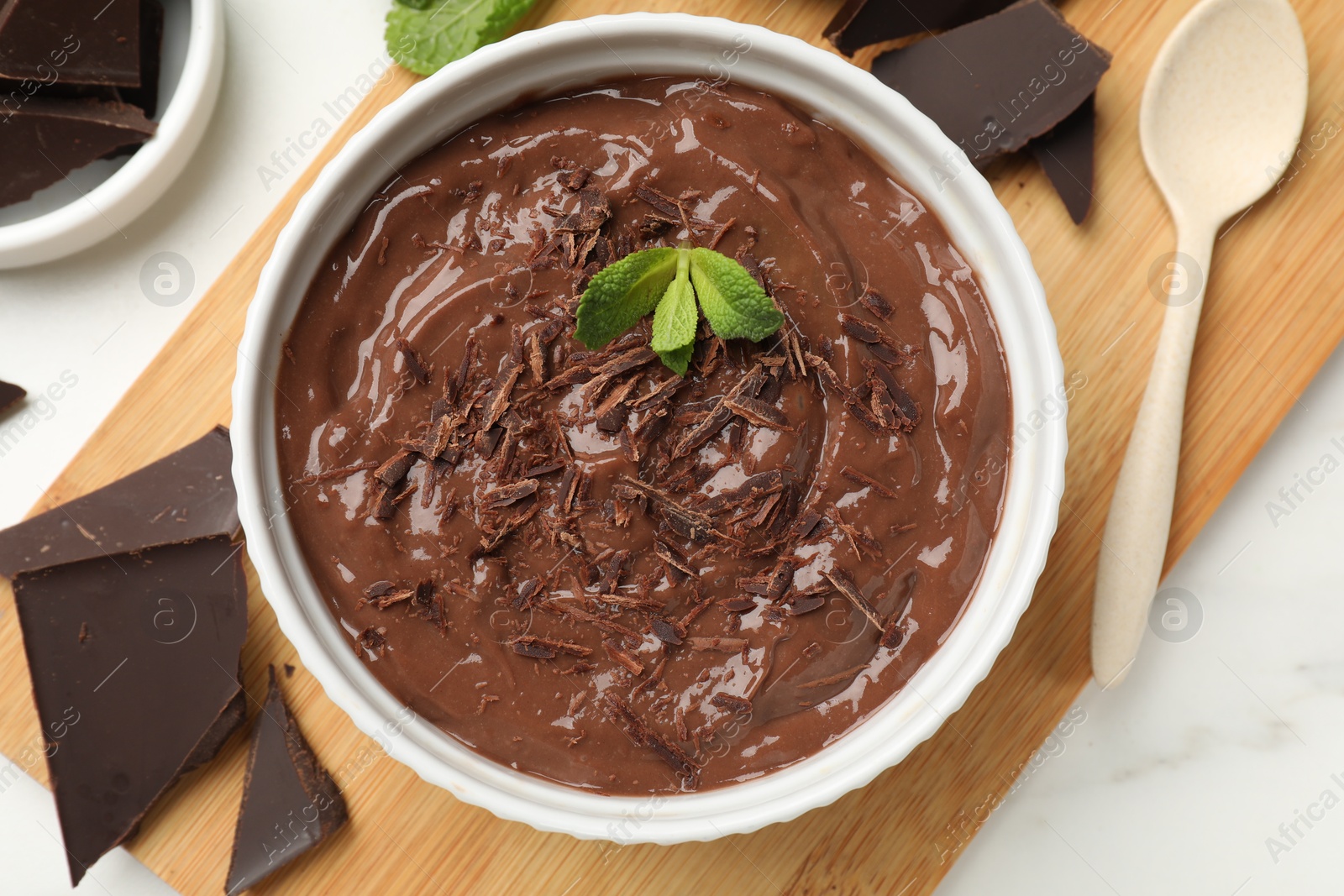 Photo of Tasty chocolate pudding in bowl served on white marble table, flat lay