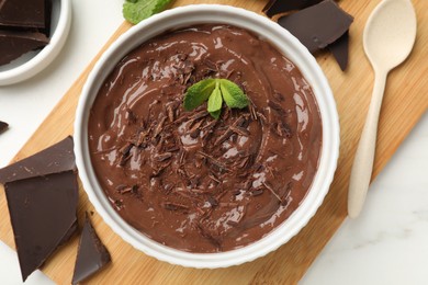 Photo of Tasty chocolate pudding in bowl served on white marble table, flat lay