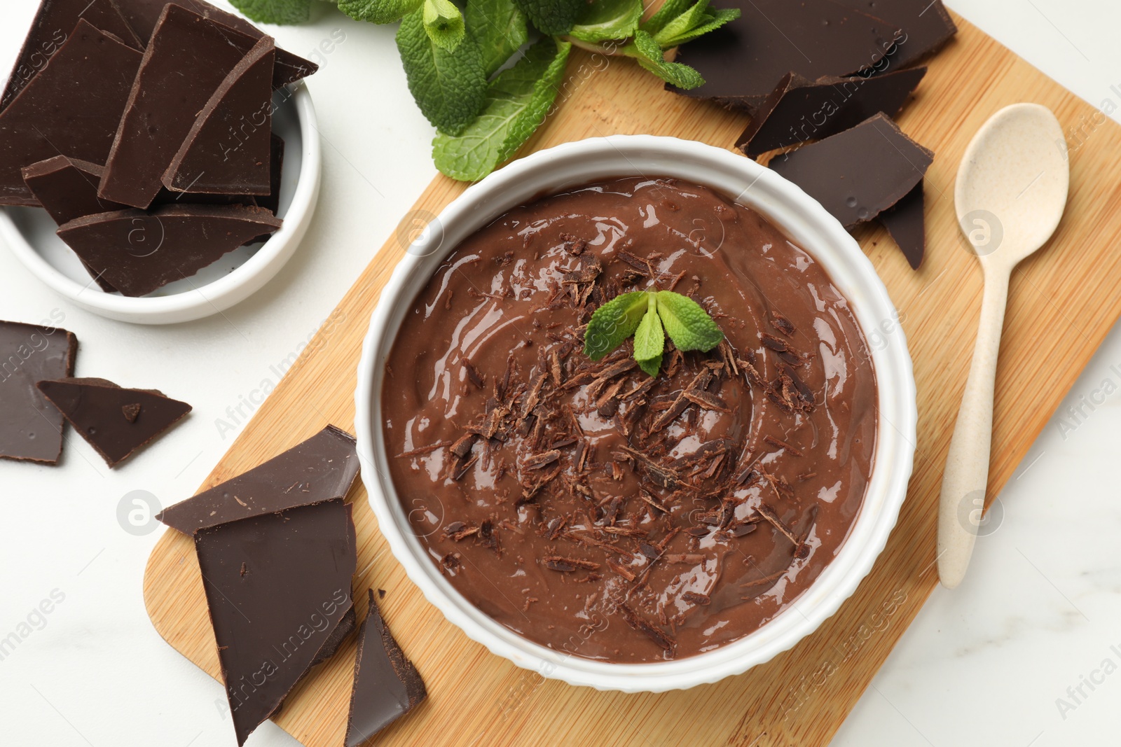 Photo of Tasty chocolate pudding in bowl served on white marble table, flat lay