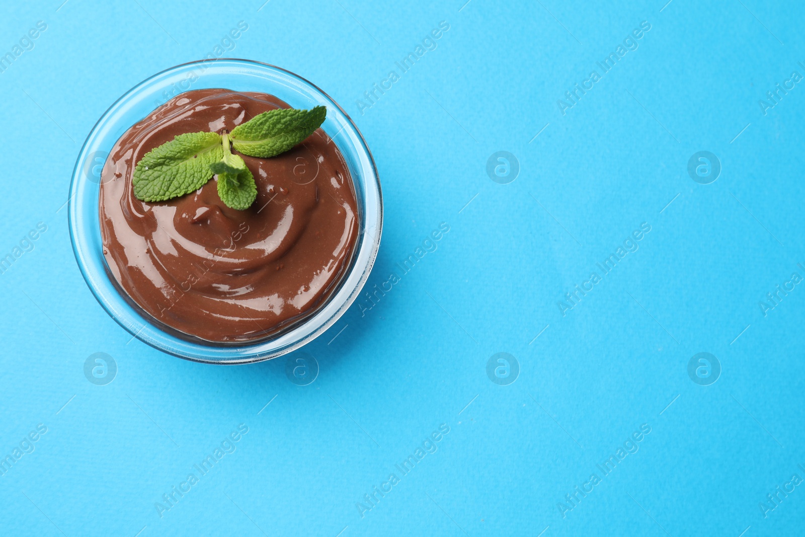 Photo of Delicious chocolate mousse in glass bowl on light blue background, top view. Space for text