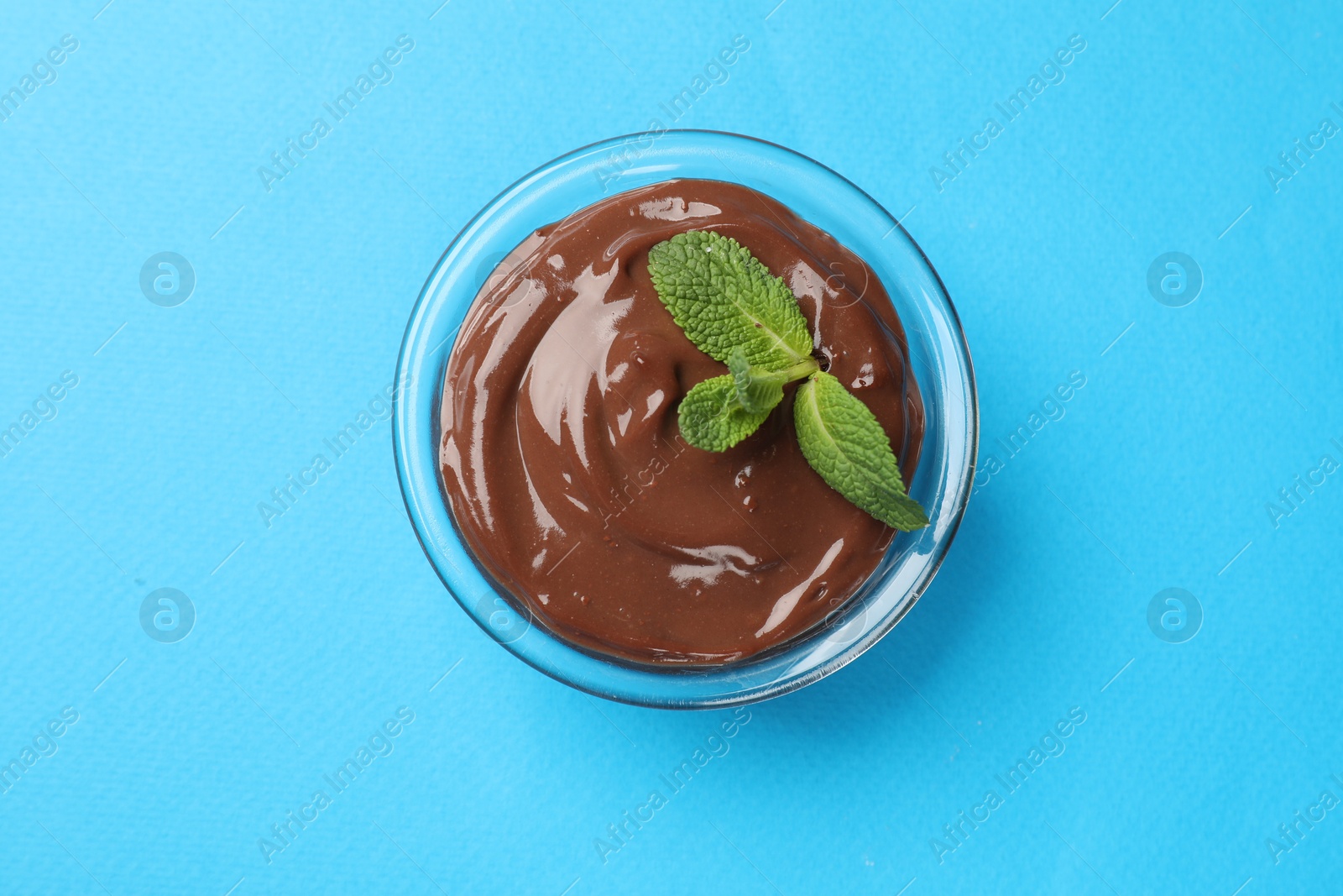 Photo of Delicious chocolate mousse in glass bowl on light blue background, top view