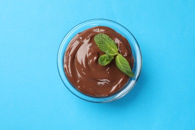 Photo of Delicious chocolate mousse in glass bowl on light blue background, top view