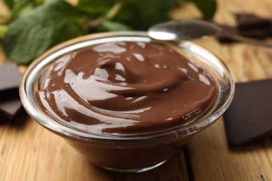 Photo of Delicious chocolate mousse in glass bowl and spoon on wooden table, closeup