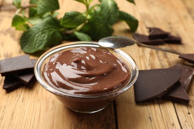 Photo of Delicious chocolate mousse in glass bowl and spoon on wooden table, closeup